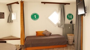 A single bedroom with a bed, a small table, a chair, a window, and a radiator. There are two green signs on the wall indicating room numbers 1 and 10.