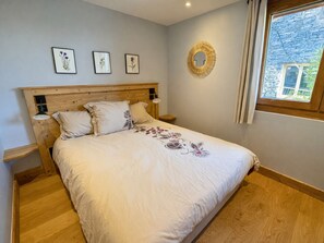 Ein Schlafzimmer mit einem hölzernen Kopfende, einem Bett mit floralem Bettbezug, Nachttischlampen und floralen Bildern in Rahmen an der Wand.