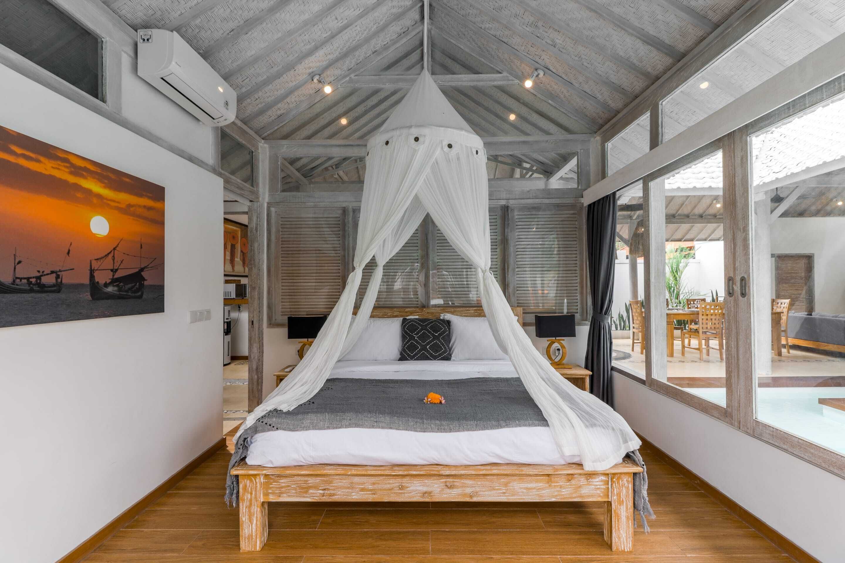 Quarto com cama de madeira, dossel branco e pintura de pôr do sol na parede.