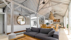 Amplia sala de estar con un sofá de madera, un espejo redondo y una mesa de comedor.