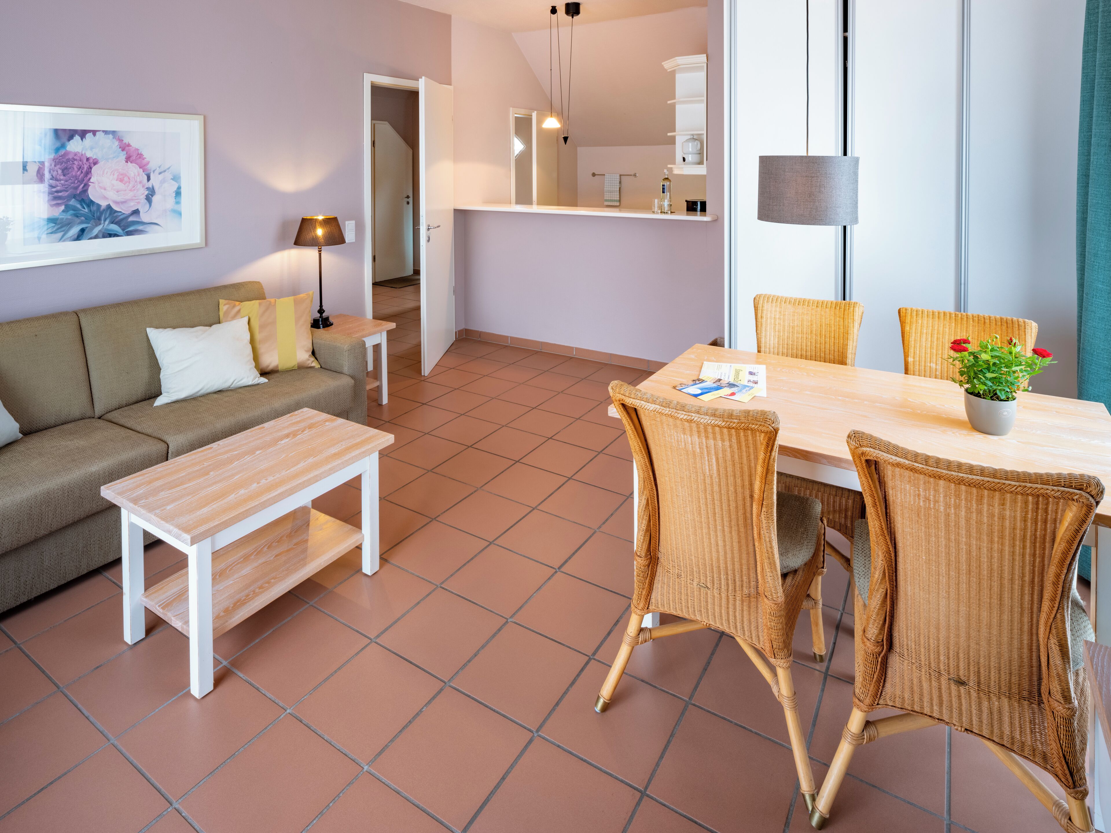 A living room with a sofa, a coffee table, and a dining area with wicker chairs and a table.