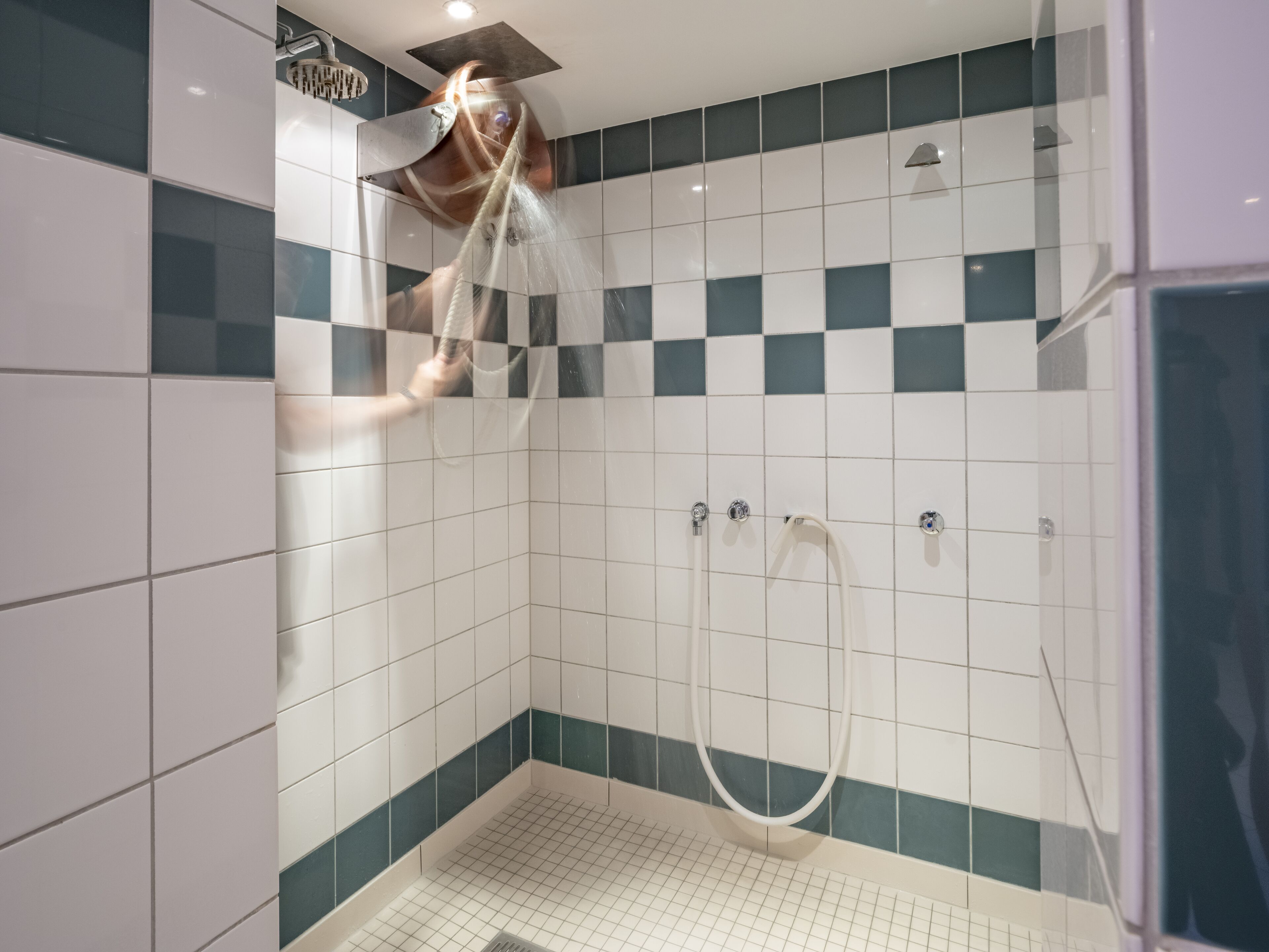 Una ducha moderna con puerta de vidrio, azulejos blancos y turquesa, y desagüe visible.