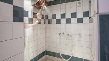 Una ducha moderna con puerta de vidrio, azulejos blancos y turquesa, y desagüe visible.