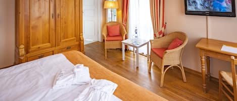 A hotel room with a large bed, a wooden wardrobe, a television, a wicker chair, and a small table.