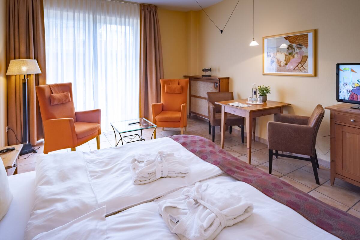 Hotellihuone, jossa on suuri sänky, kaksi nojatuolia, työpöytä, televisio ja taulu seinällä.