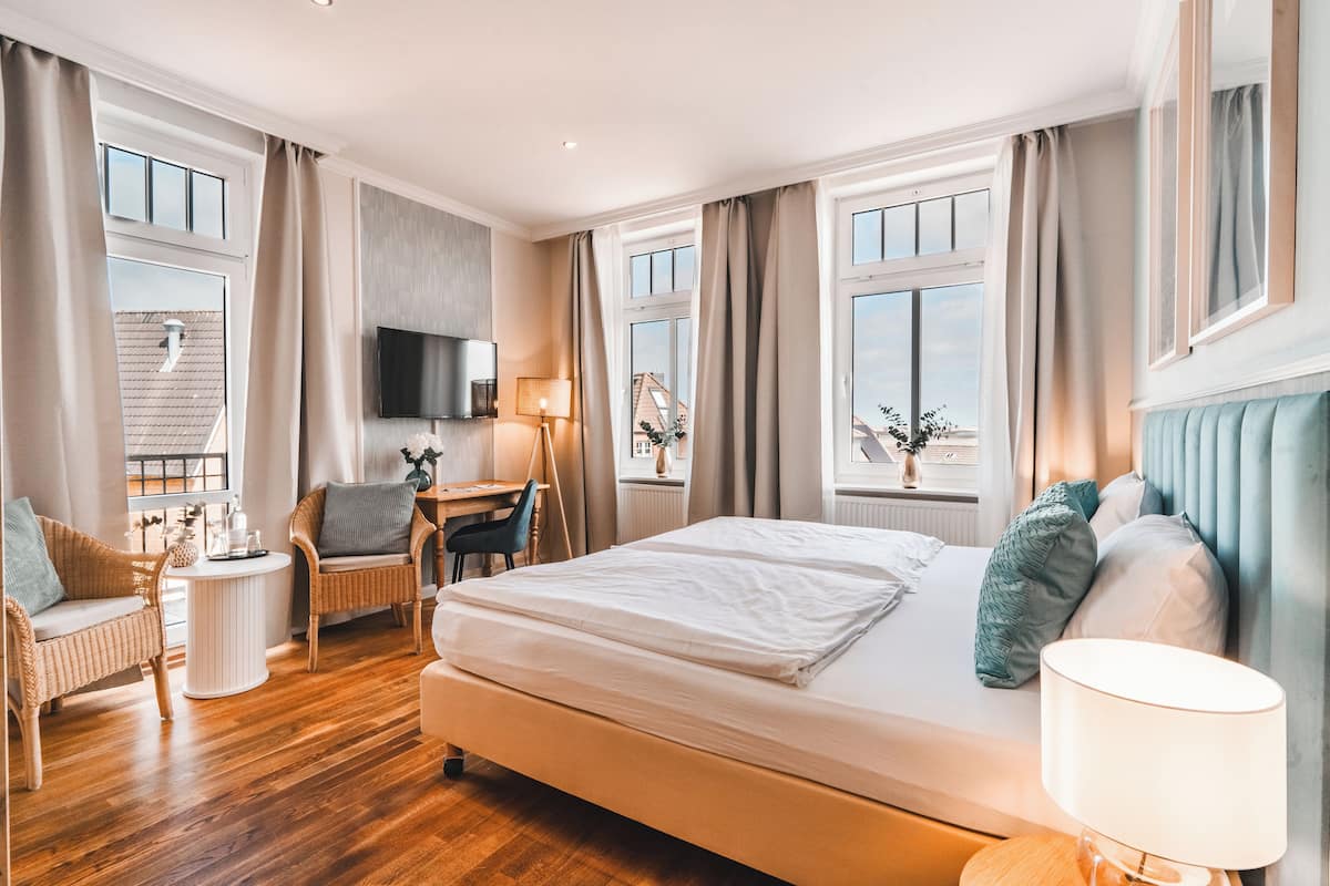 Hotellihuone, jossa on suuri sänky, kaksi tuolia, työpöytä, televisio ja suuret ikkunat.