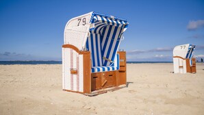 Una silla de playa con estampado a rayas y el número 79, ubicada en una playa arenosa con un cielo azul despejado de fondo.
