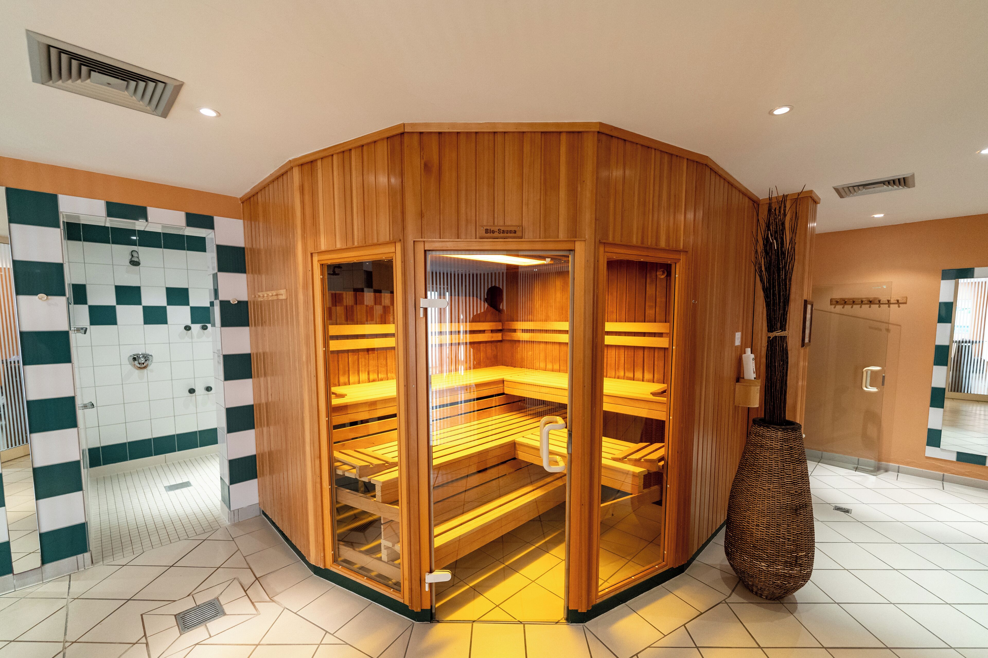 A sauna room with wooden walls and glass doors, a checkered shower area, and a large vase.