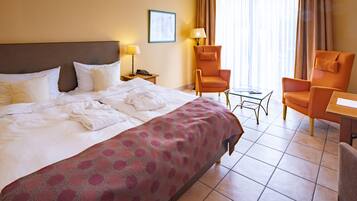 Ein Hotelzimmer mit einem großen Bett, zwei Sesseln, einem kleinen Tisch und einem Nachttisch mit einer Lampe.