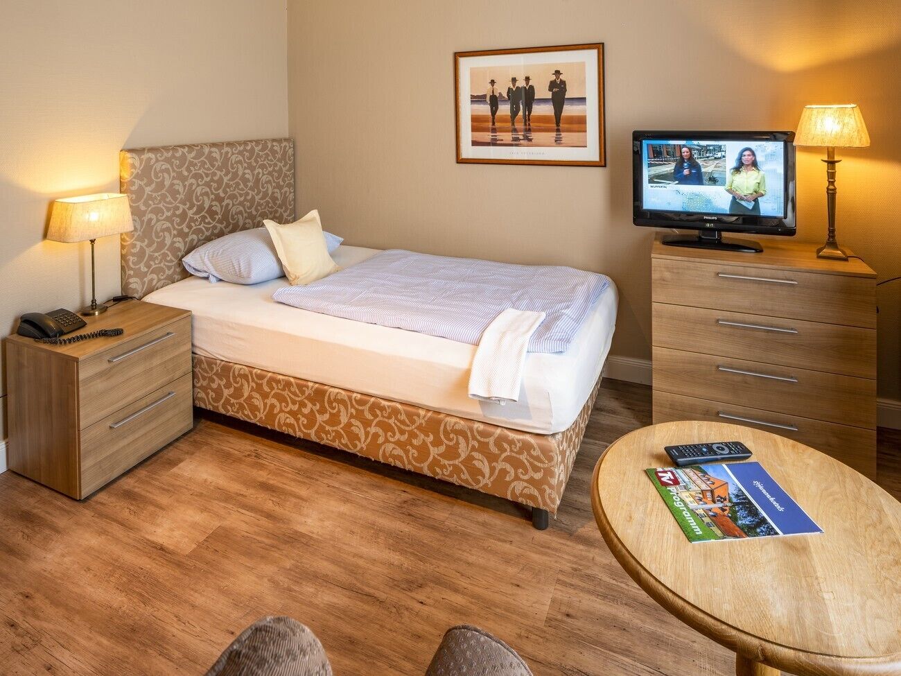 Une chambre d’hôtel comprenant un lit, des tables de chevet, une télévision, une lampe et une petite table avec une télécommande et des brochures.