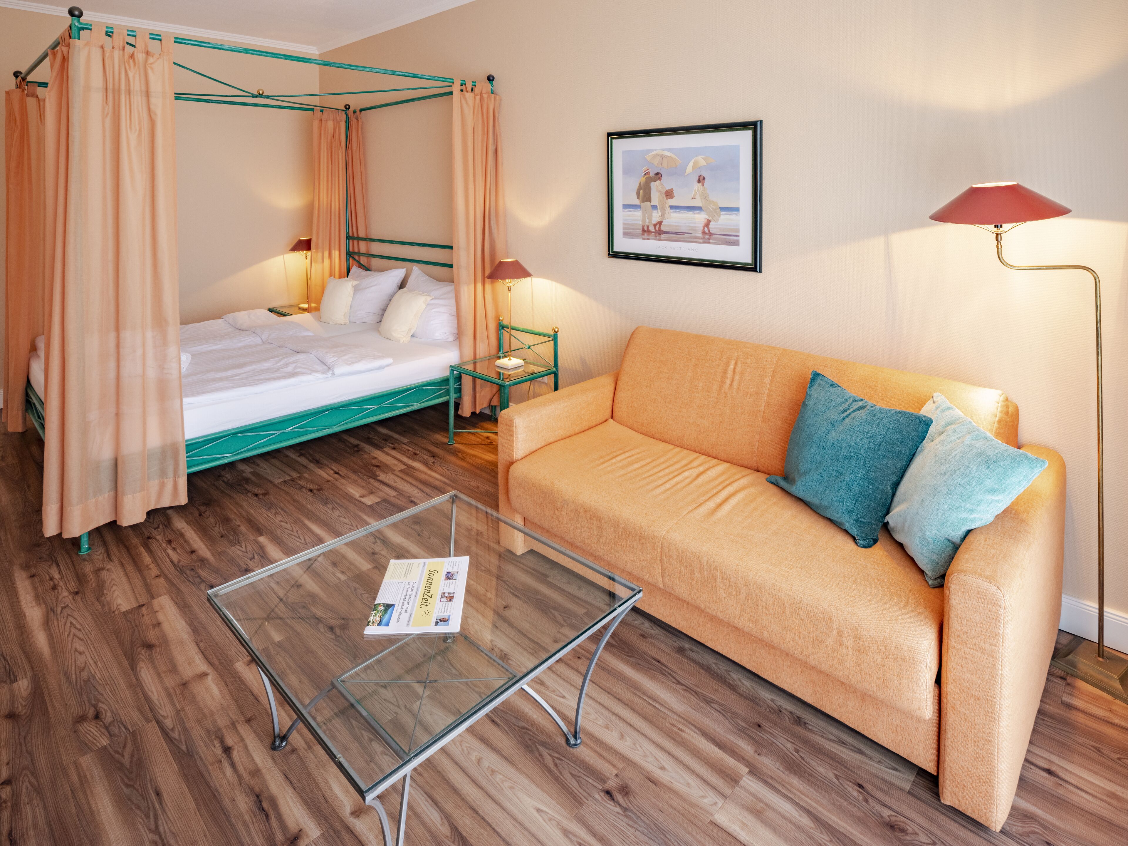 Un dormitorio con cama con dosel, un sofá, una mesita de centro de cristal y un cuadro enmarcado en la pared.