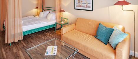 Un dormitorio con cama con dosel, un sofá, una mesita de centro de cristal y un cuadro enmarcado en la pared.