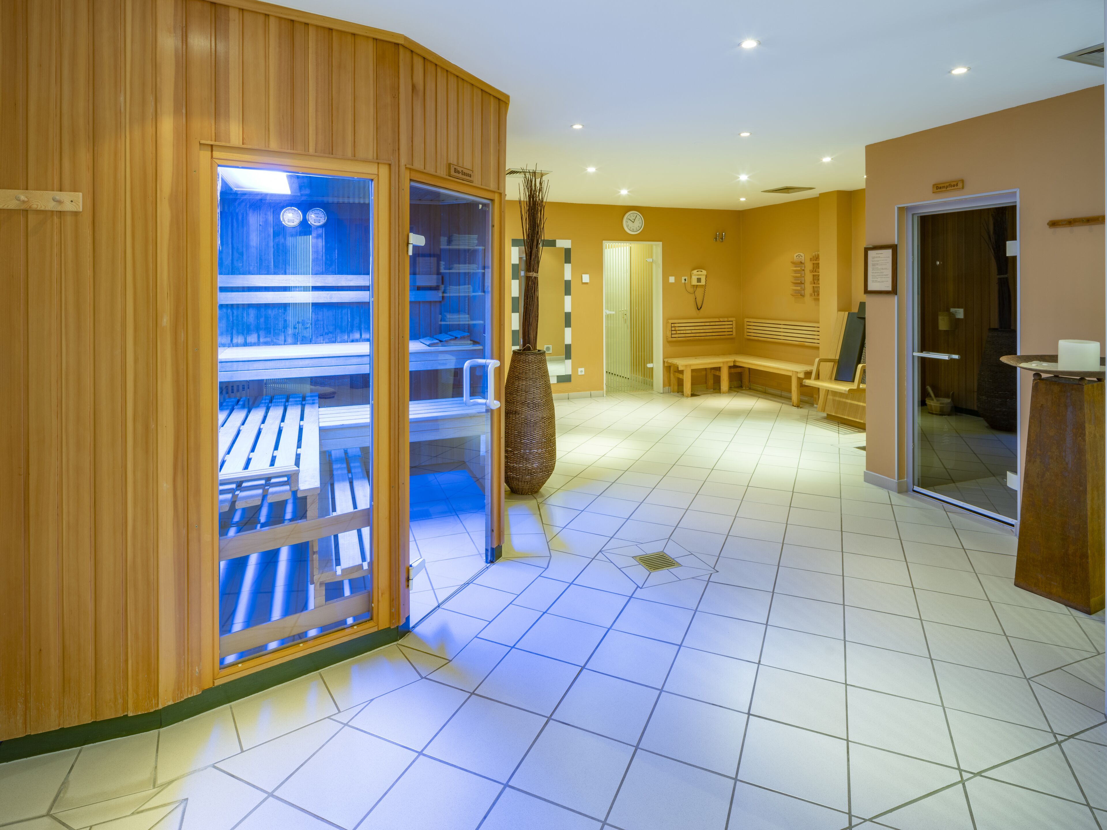 A spa area with wooden walls, a glass door leading to a massage room, a bench, and a reception desk.
