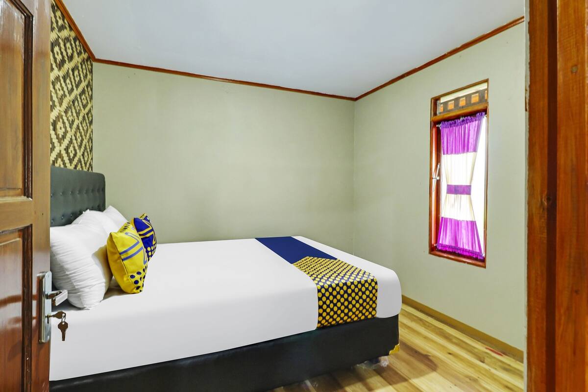 Un dormitorio con cama, ventana con cortinas moradas, pared estampada y suelo de madera.