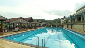 A swimming pool with lounge chairs and umbrellas, surrounded by buildings with a stone facade and a covered area with seating. - Hotel O Desa Wisata Guranteng (Guranteng)