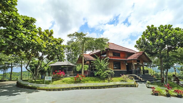 A two-story building with a red-tiled roof, surrounded by lush greenery and a white picket fence. - Hotel O Desa Wisata Guranteng (Guranteng)