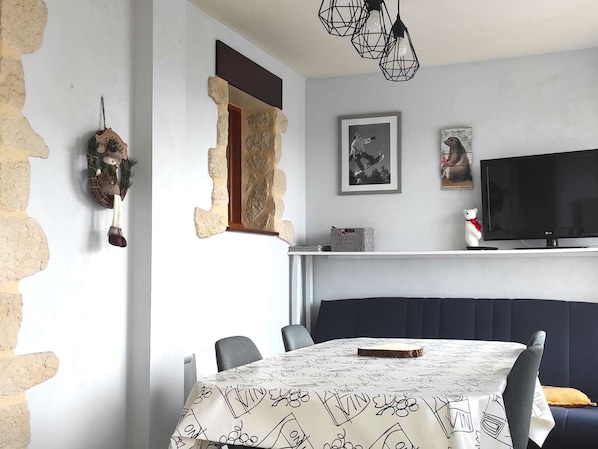 Un comedor con una mesa cubierta por un mantel estampado, un televisor sobre un mueble bajo y una pared de piedra con un adorno.