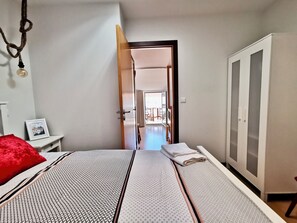 A bedroom with a bed, a wardrobe, a bedside table with a picture, and a door leading to another room.