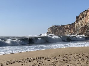 A beach with waves crashing onto the shore, a sandy beach, and a cliff with buildings on top.