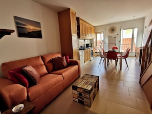 A living room with a brown sofa, a dining area with a table and chairs, a kitchen with wooden cabinets, and a balcony with a view.