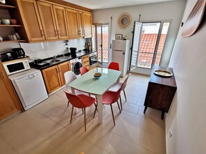 A compact kitchen with wooden cabinets, a dining table with red chairs, a washing machine, and a refrigerator.