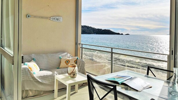 A cozy balcony with a sofa, a small table, and a view of the sea.