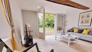 A modern living room with a sofa, coffee table, and a door leading to an outdoor area. - Family Retreat with Garden, Near Leisure Activities (Saint-Poix)