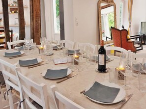 Une table à manger dressée avec des assiettes, des verres et une bouteille de vin, entourée de chaises blanches.