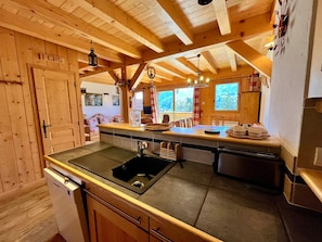 A wooden cabin interior with a kitchen area featuring a sink, stove, and dining space.