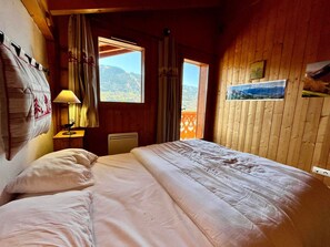 Une chambre à coucher comprenant un lit, une table de chevet, une lampe, une fenêtre avec des rideaux et un tableau accroché au mur.