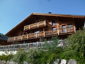 Un chalet en bois doté de plusieurs balcons, un mur de pierre au premier plan et un ciel bleu dégagé.