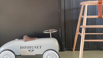 A white toy car with "HØJHUSET" written on it, a wooden ladder, and a dark wall.