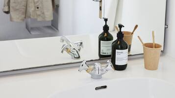 A bathroom with a white sink, a mirror, a bottle of Meraki soap, a toothbrush holder, and a hanging towel.