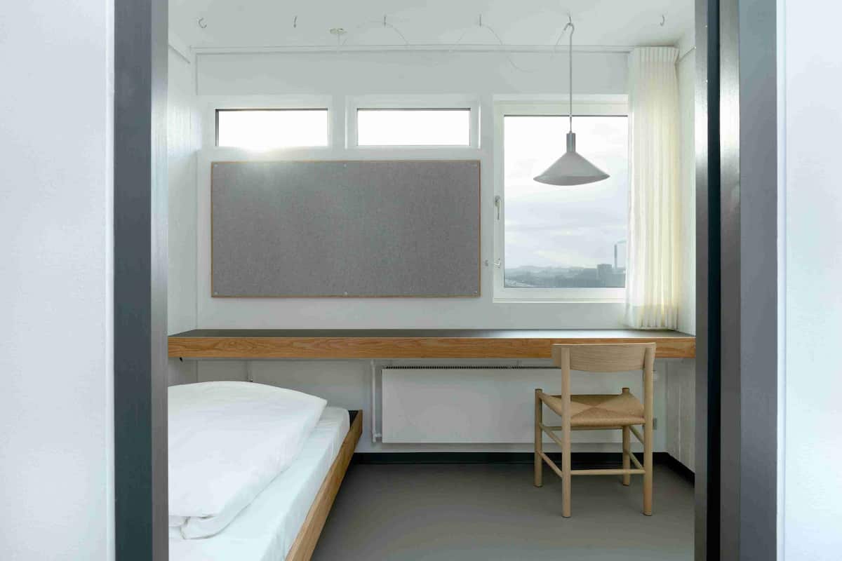 A bedroom with a bed, a desk, a chair, a window, and a radiator.