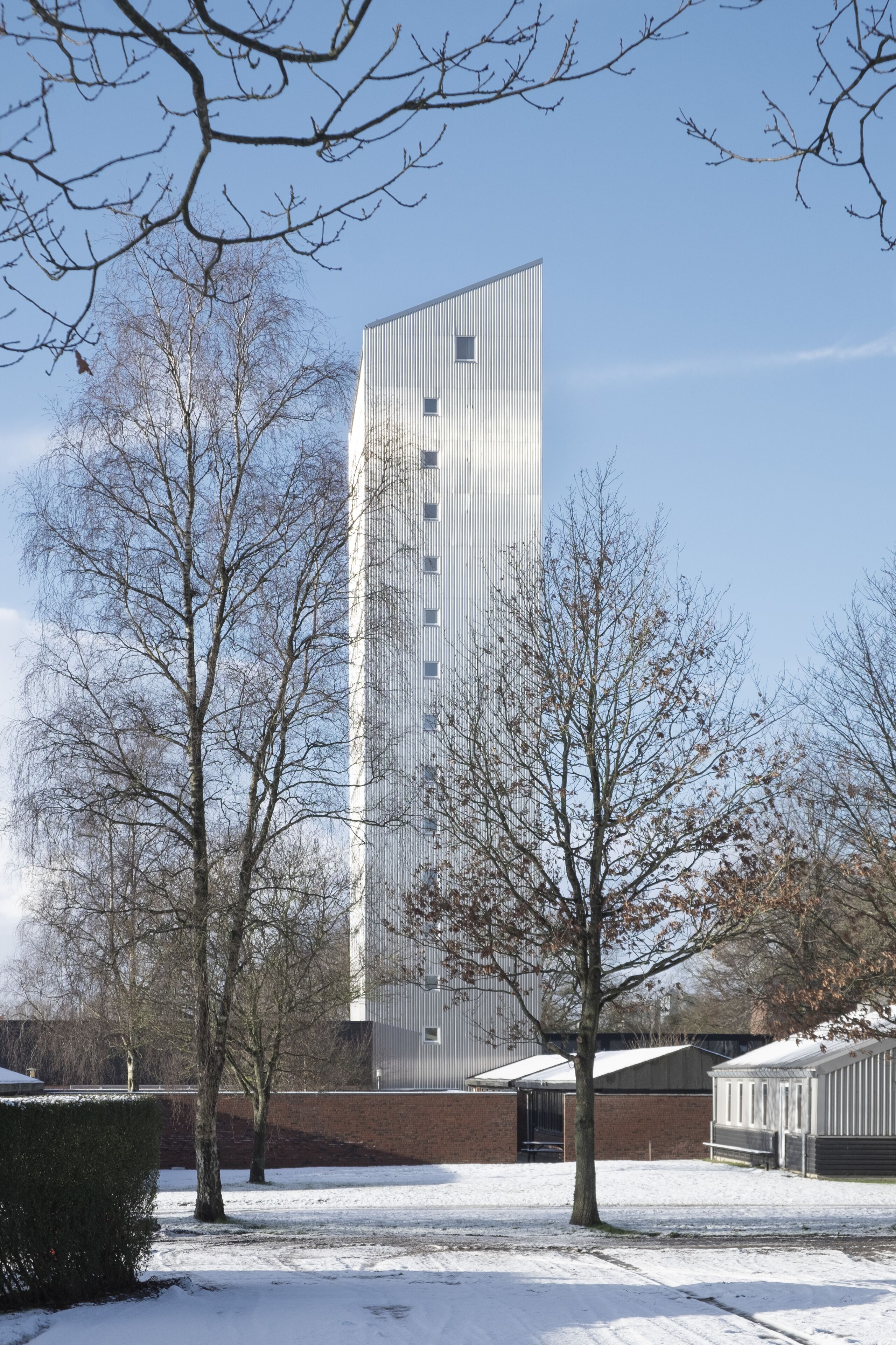 Un bâtiment moderne à la conception verticale, entouré d’arbres sans feuilles et d’un sol recouvert de neige.