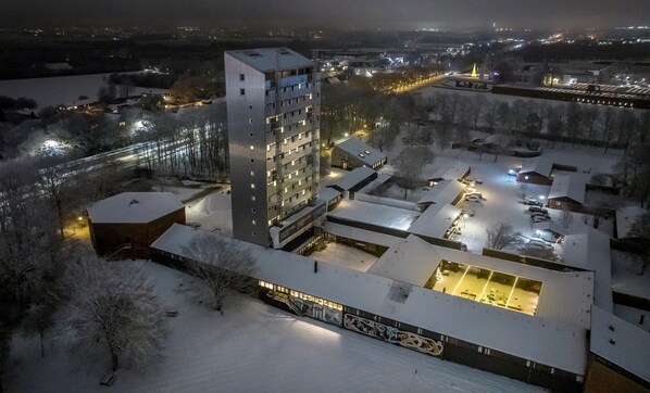 Un edificio alto con varios pisos, un área de estacionamiento y alrededores cubiertos de nieve.