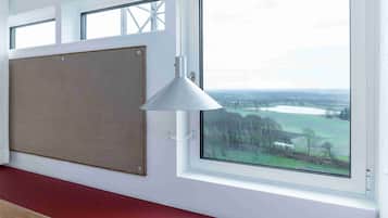 A room with a large window, a corkboard on the wall, and a white pendant light.
