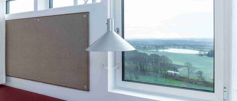 A room with a large window, a corkboard on the wall, and a white pendant light.