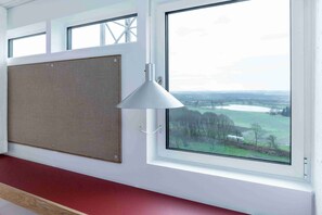 A room with a large window, a corkboard on the wall, and a white pendant light. - Højhuset Kulturhotel (Herning)