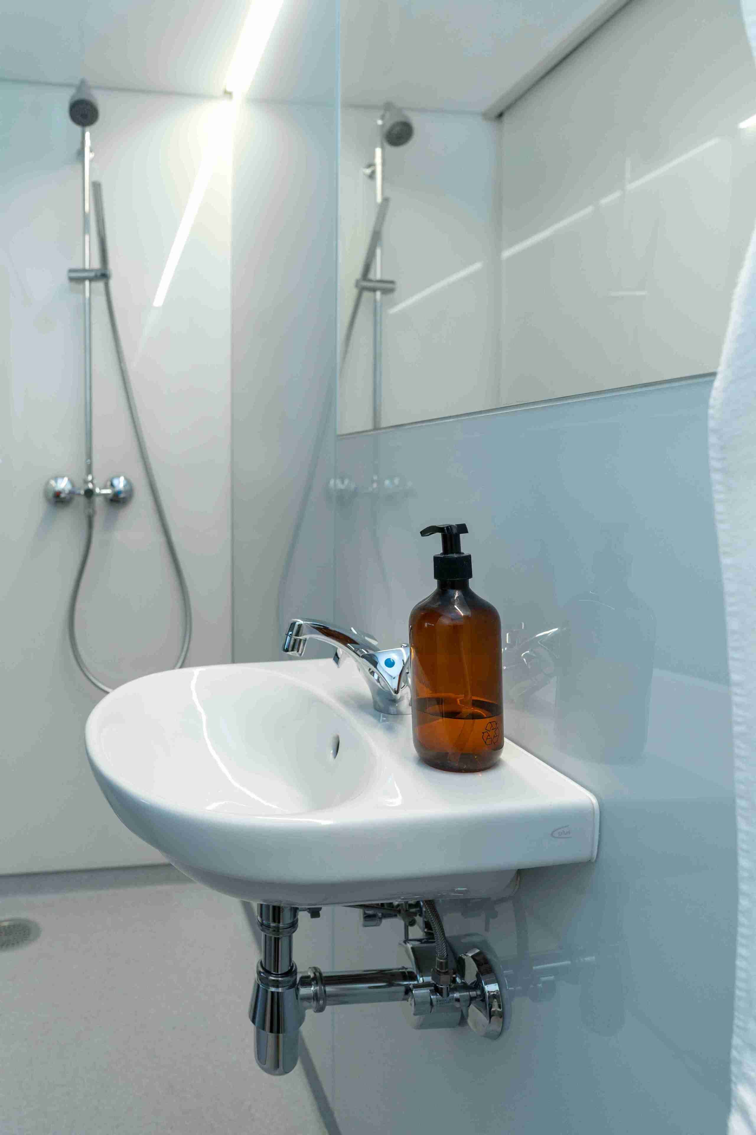 Un baño con lavamanos blanco, grifo cromado y cabezal de ducha de mano.