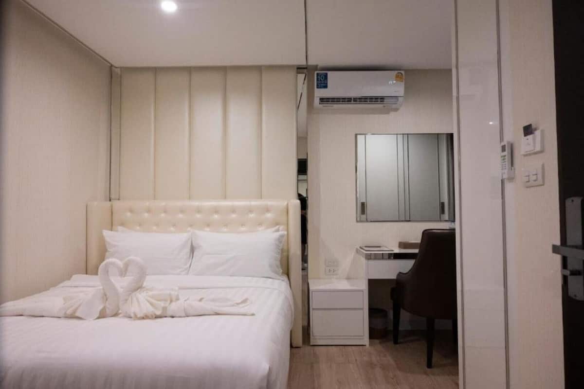 A hotel room with a bed, a desk, and a chair. There is an air conditioning unit above the desk.