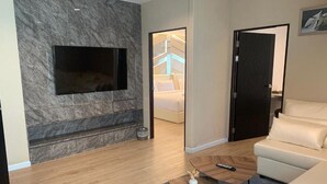 Un saló modern amb televisió de pantalla plana penjada a una paret de marbre, una taula de centre de fusta amb un vas i un sofà blanc.