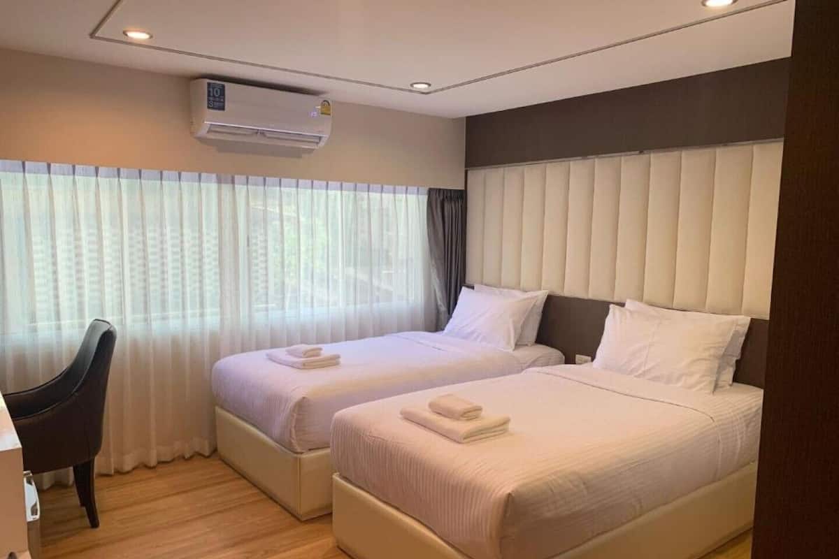 A hotel room with two beds, a desk, and an air conditioning unit.