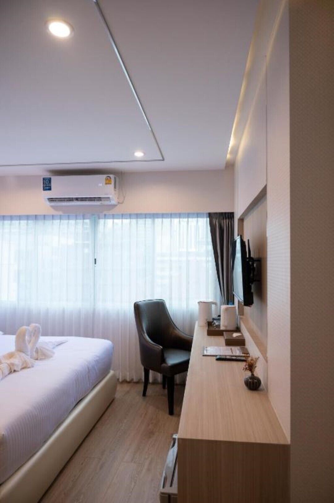 A hotel room with a bed, a desk, a chair, an air conditioning unit, and a window with curtains.
