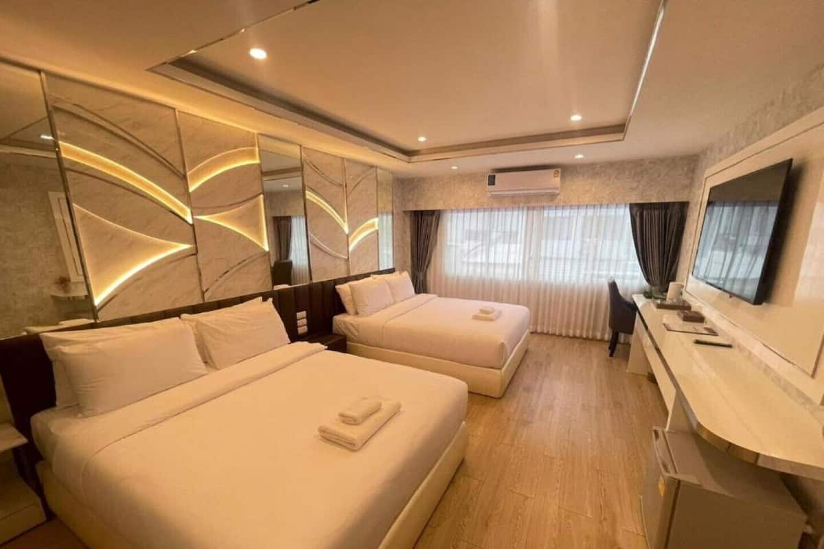 A hotel room with two beds, a desk, a TV, and a mirror.