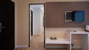 Una habitació d'hotel moderna amb sòl de fusta, una taula consola blanca, un televisor de pantalla plana fixat a la paret i una porta que dóna a una altra habitació.