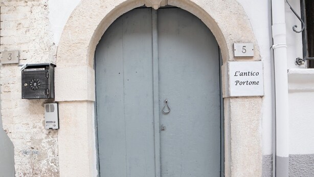 A gray door with an arched stone frame, a mailbox, and a sign reading "L'antico Portone".