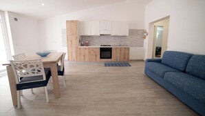 A modern kitchen with wooden cabinets, a dining table with chairs, and a blue sofa.