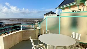 Ein Balkon mit einem runden Tisch und vier Stühlen, mit Blick auf einen Strand und eine entfernte Küstenlinie.
