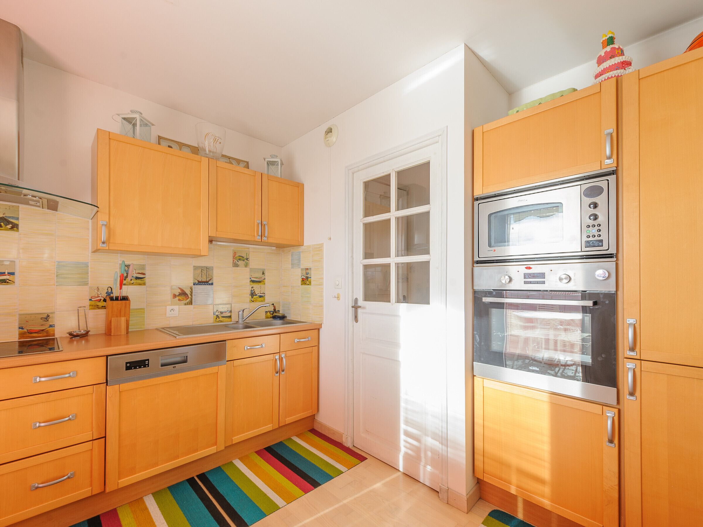 A kitchen with wooden cabinets, a stainless steel oven, and a colorful striped rug.